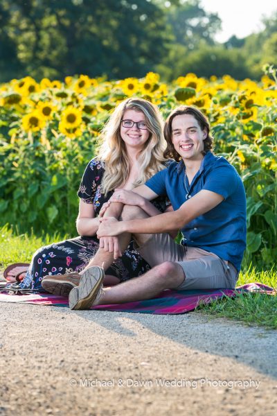picture of engaged couple sitting on blanket by sunflower field